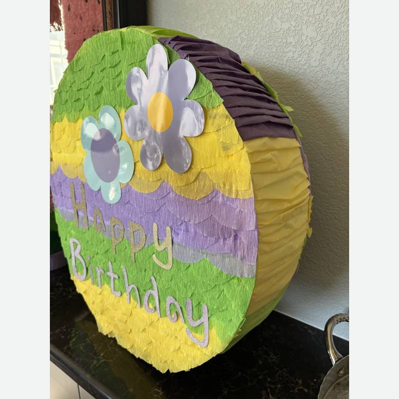 A round pull-string piñata in green, purple and yellow with a paper flower
